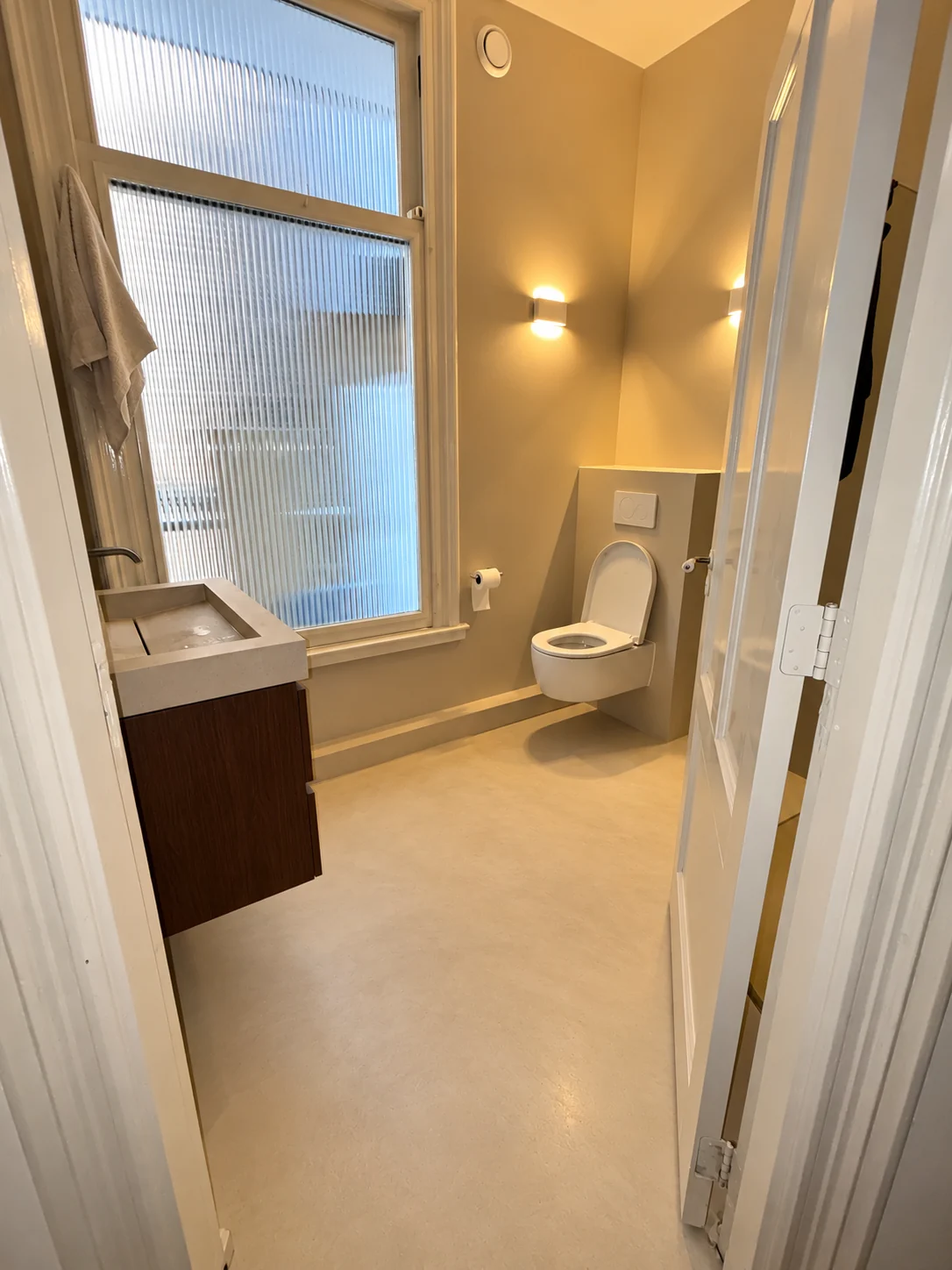 Toiletruimte met warm licht, wandtoilet en klein wastafelmeubel