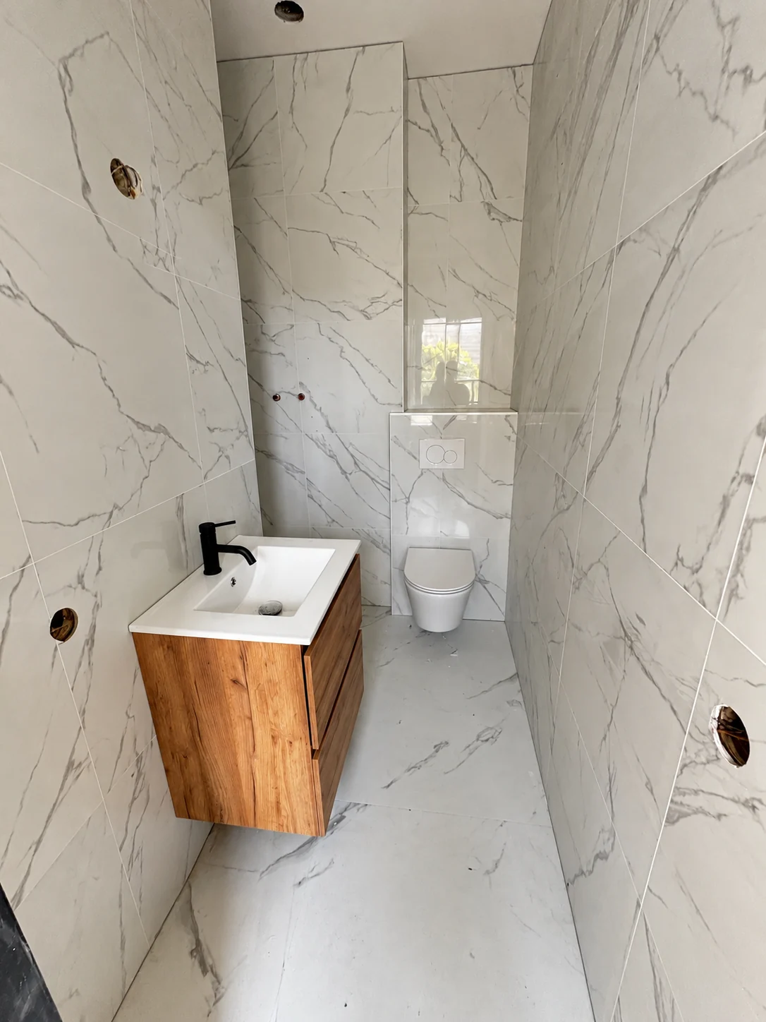 Marmerlook toiletruimte met houten wastafelmeubel en hangend toilet tijdens de werkzaamheden